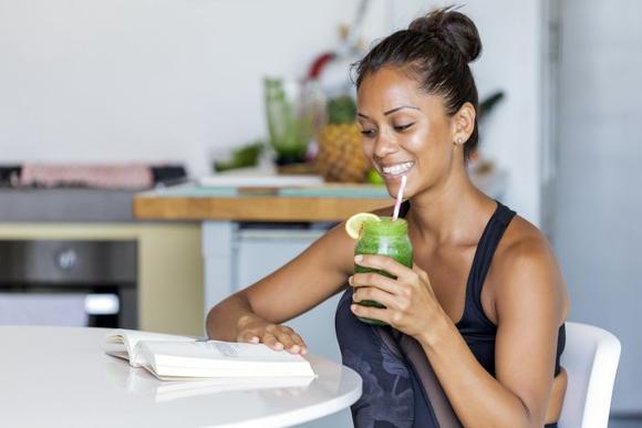 Vibrant woman drinking a green smoothie while partaking in good nutritional practices.
